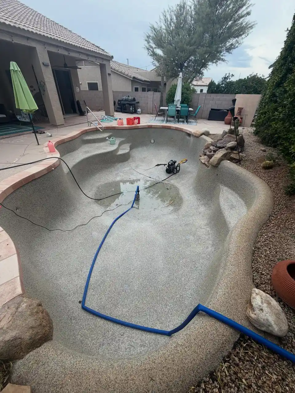 A drained pool with a hose and pump on the bare plaster floor