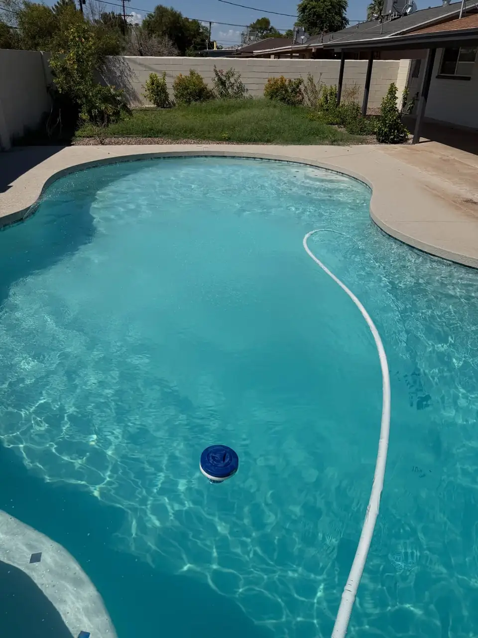 Clear pool water over a white plaster floor with a cleaner hose